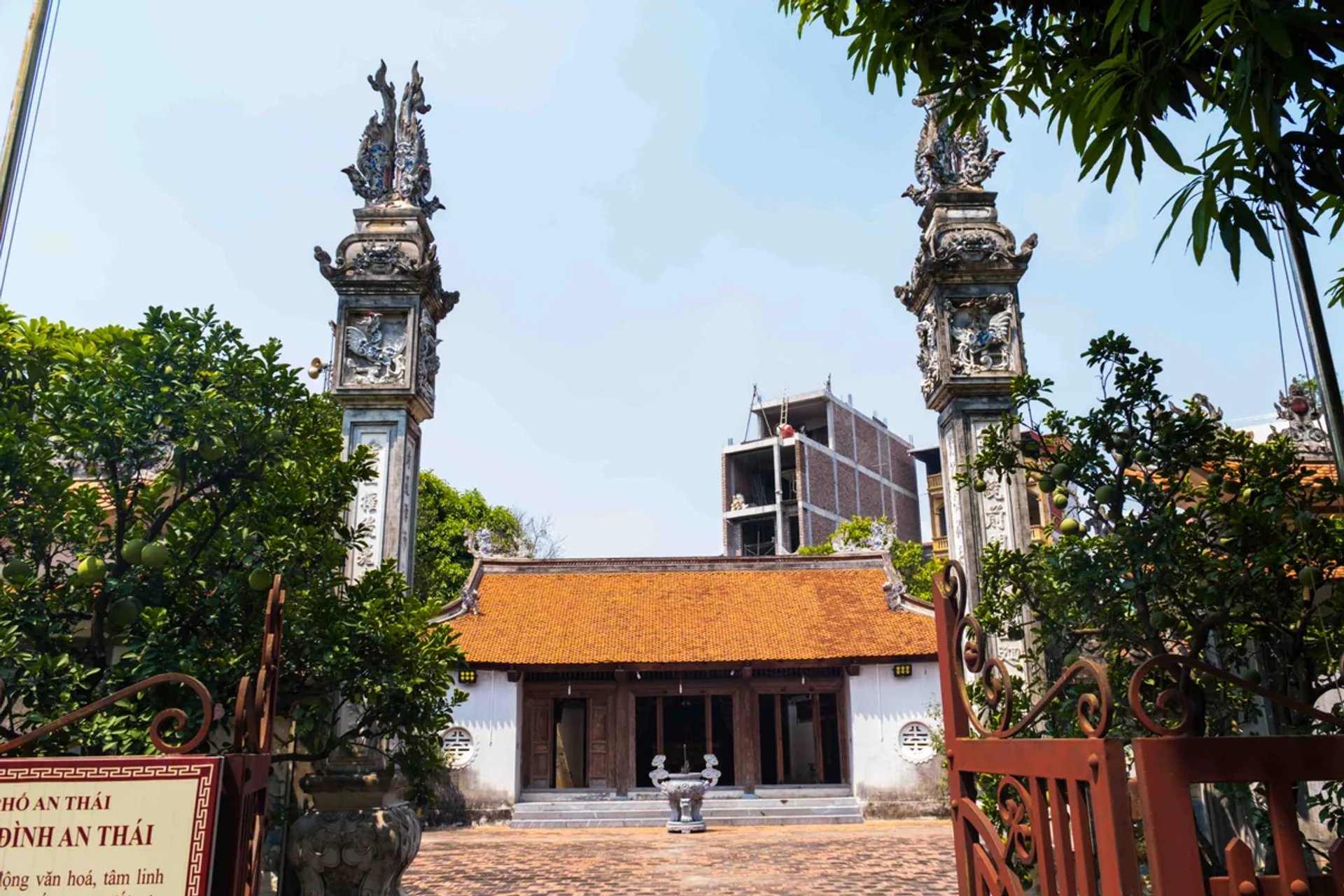 Trụ biểu và lối vào đình nhìn ra sân gạch đỏ rộng rãi
