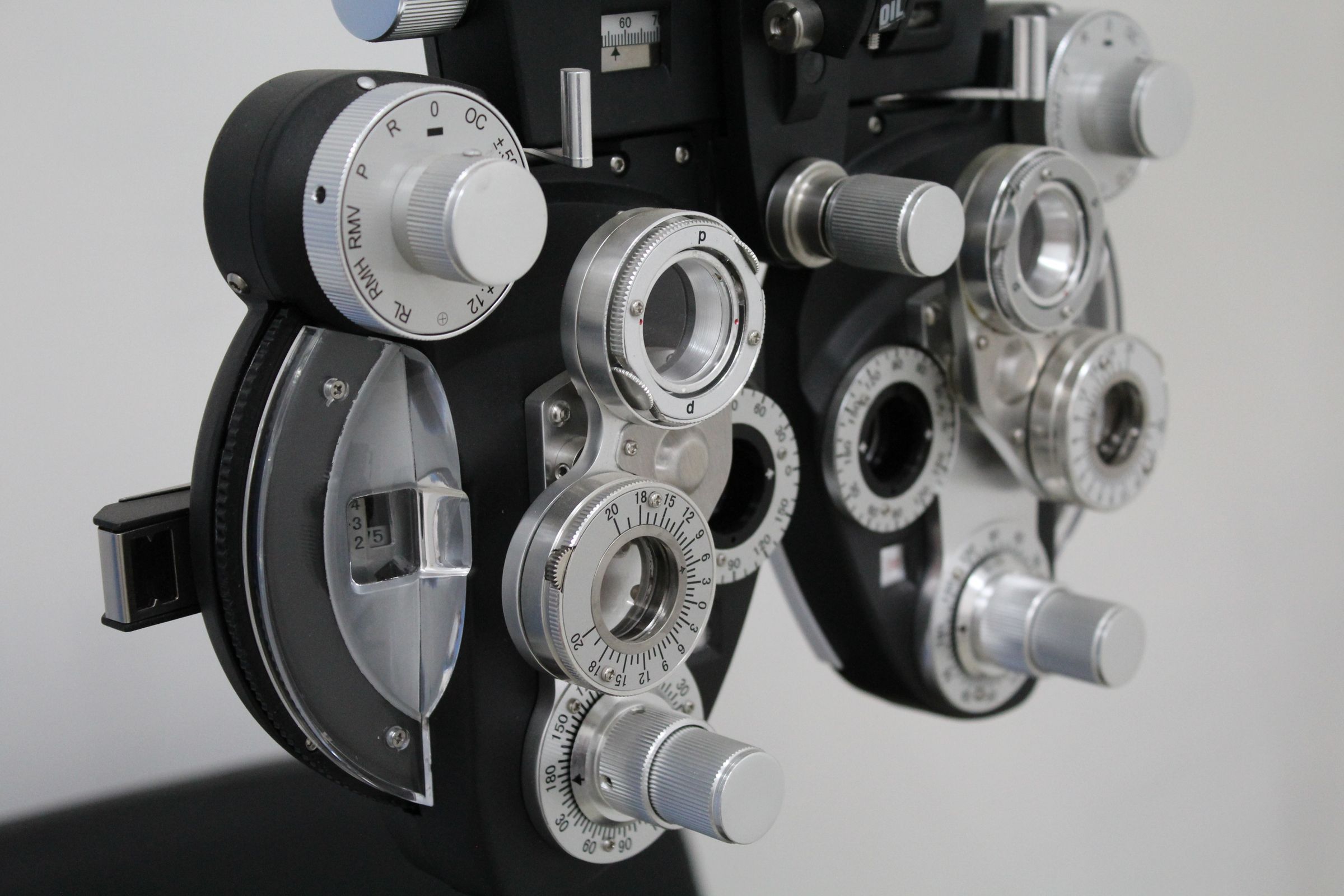 Close-up of a phoropter, the lens device used in eye exams, against a white wall.