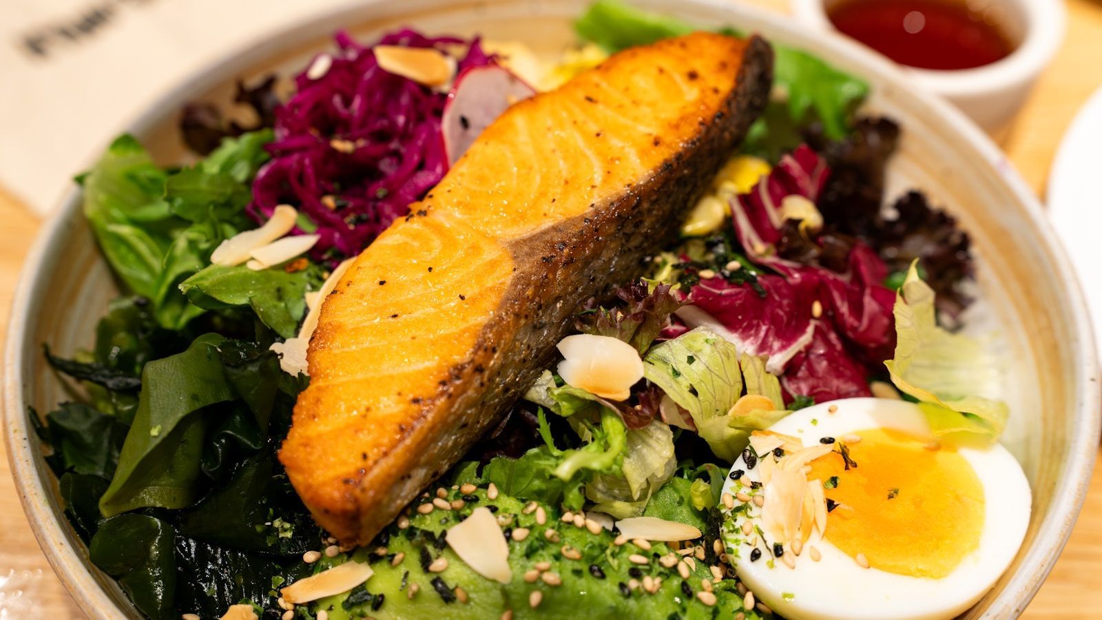 A bowl of seared salmon over mixed greens, avocado and a soft-boiled egg