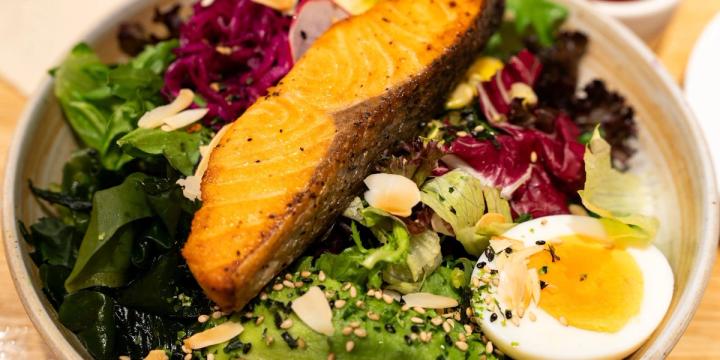 A bowl of seared salmon over mixed greens, avocado and a soft-boiled egg