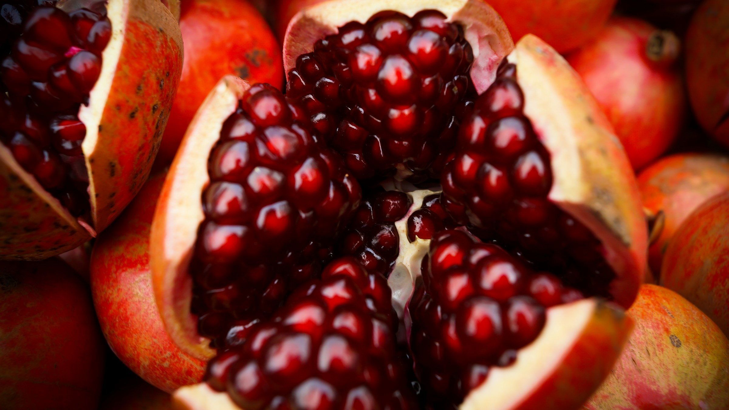 A pomegranate split open to show its packed red arils, resting on a pile of whole fruit