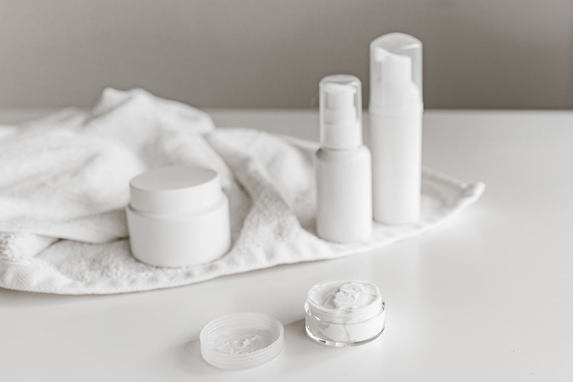 White cream jars, pump bottles and an open jar of cream on a white towel.
