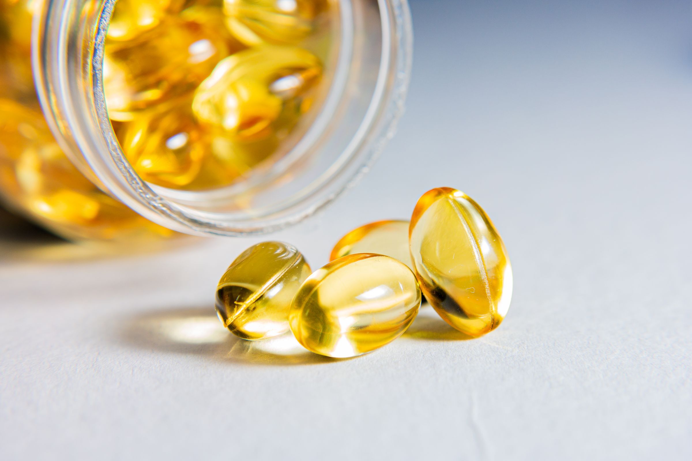 Golden softgel capsules spilling from a clear glass jar onto a light surface.