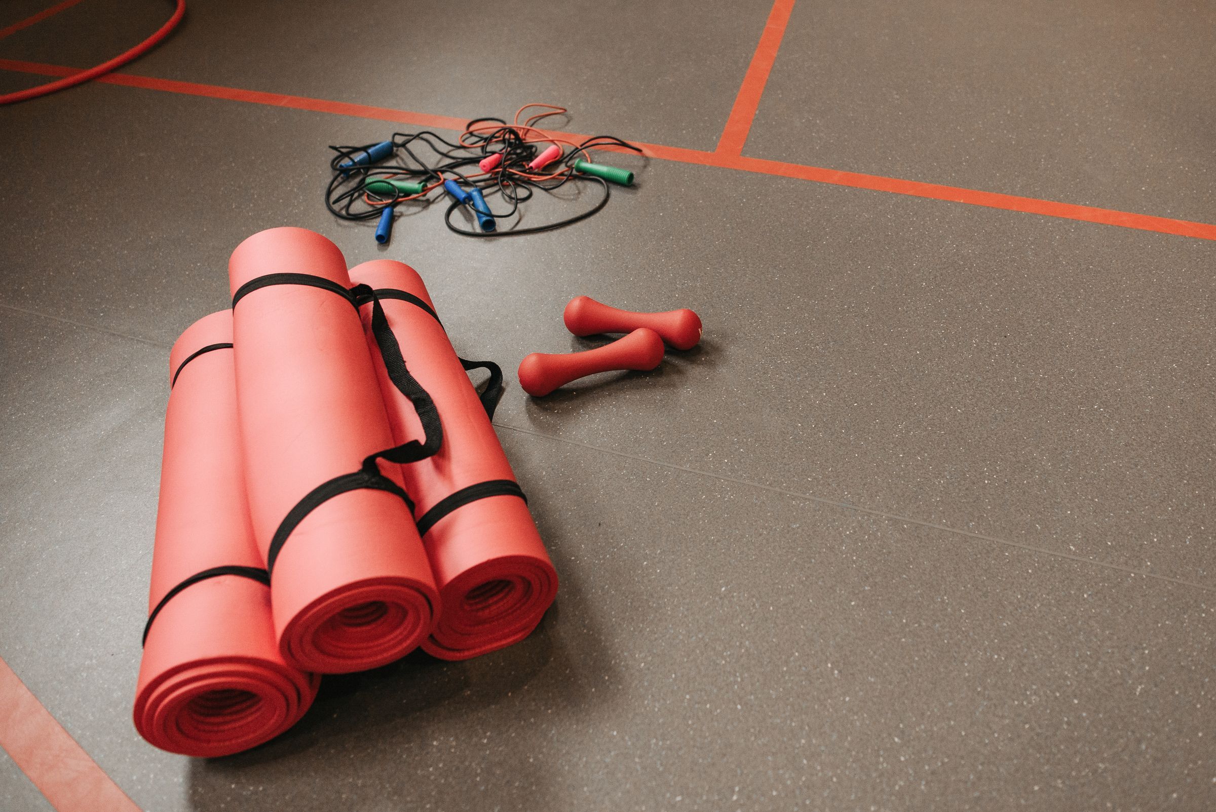 Rolled exercise mats, jump ropes and hand weights on a gym floor