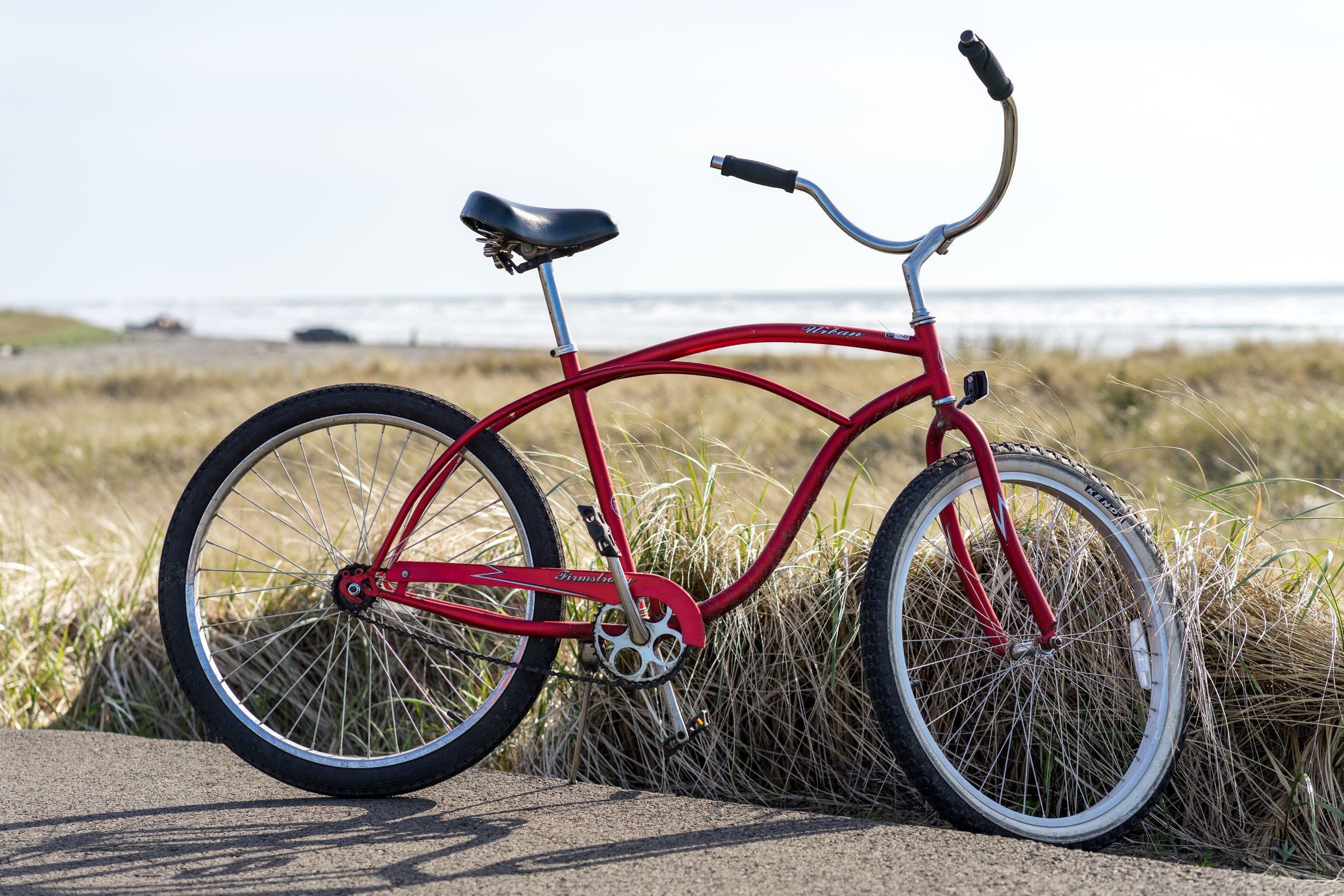 A red bicycle parked beside a coastal path with the ocean behind it