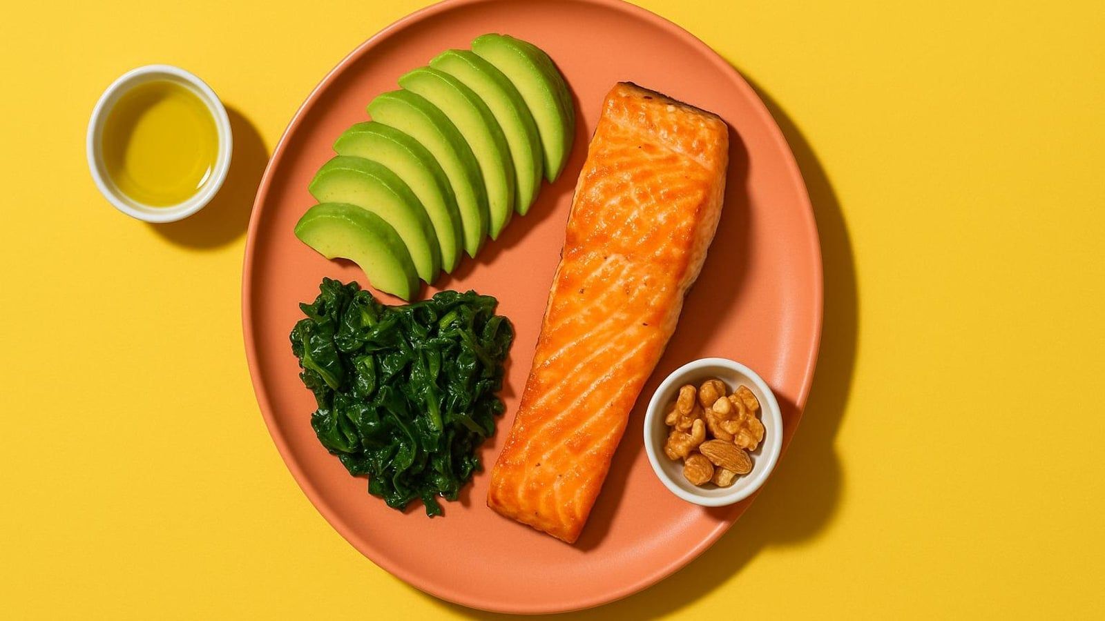 Overhead of a keto plate: salmon, avocado and greens with olive oil and nuts on a yellow surface