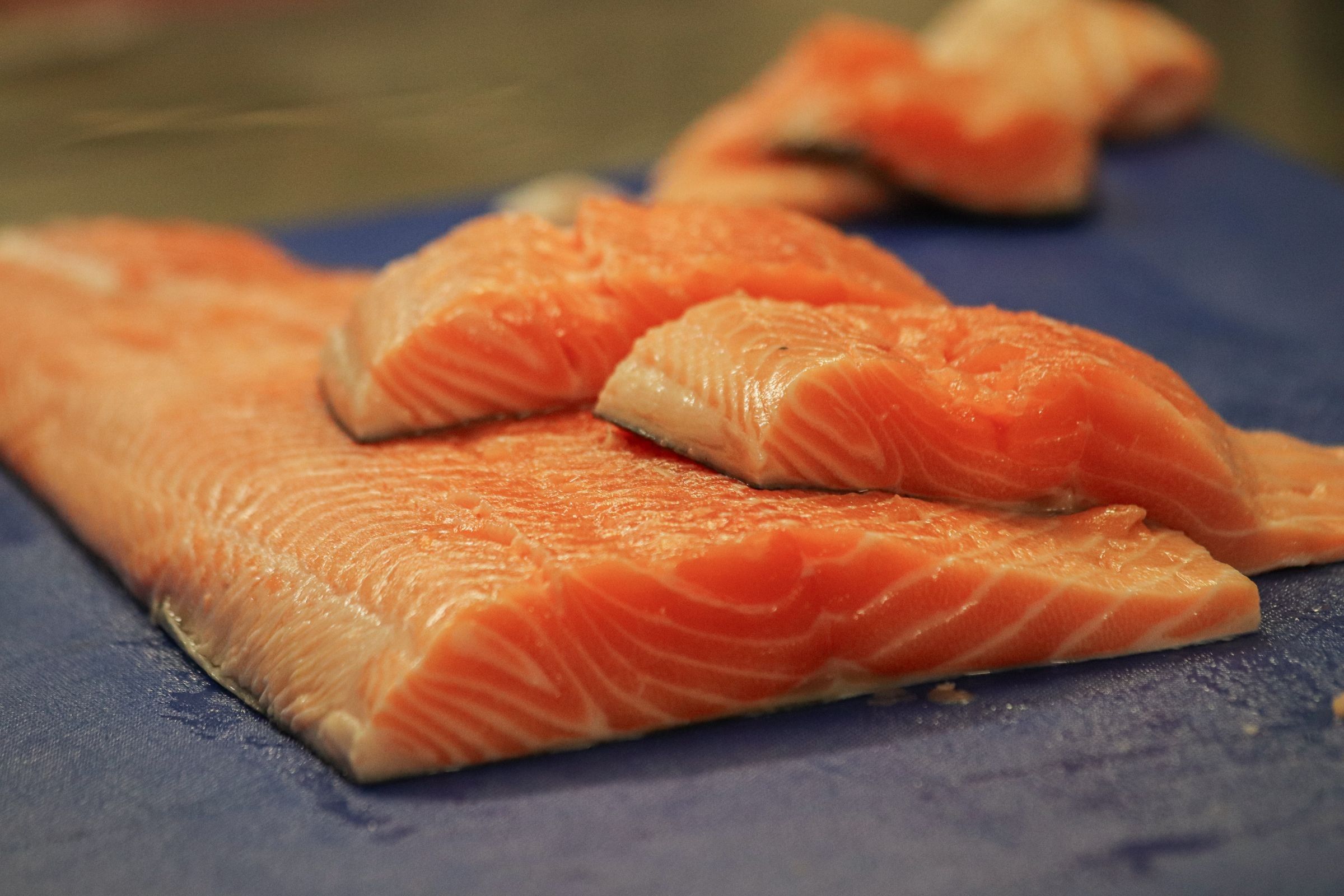 Raw salmon fillets on a blue cutting board.
