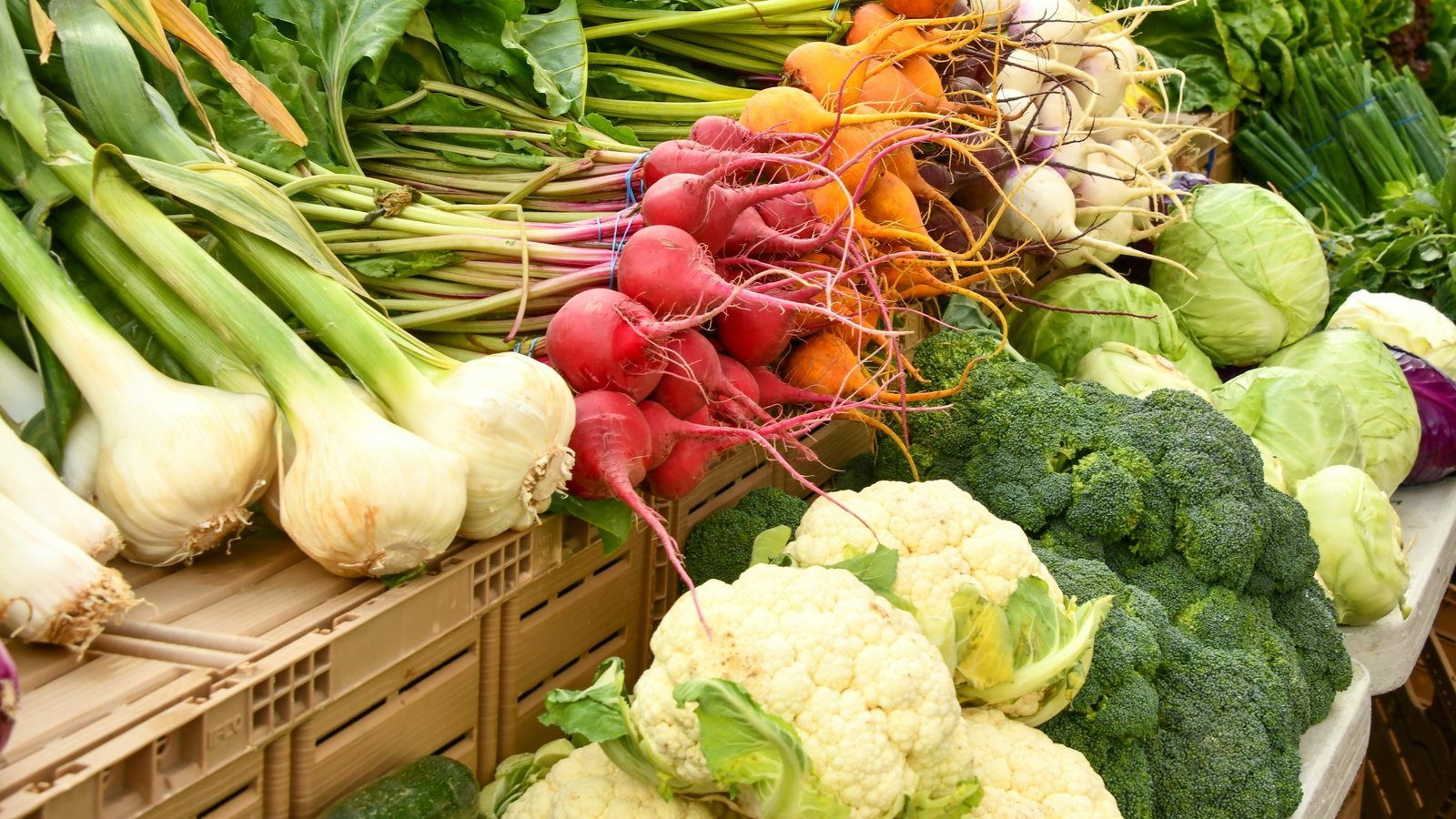 Spring onions, radishes, beets, cauliflower and broccoli stacked on a farmers market stall
