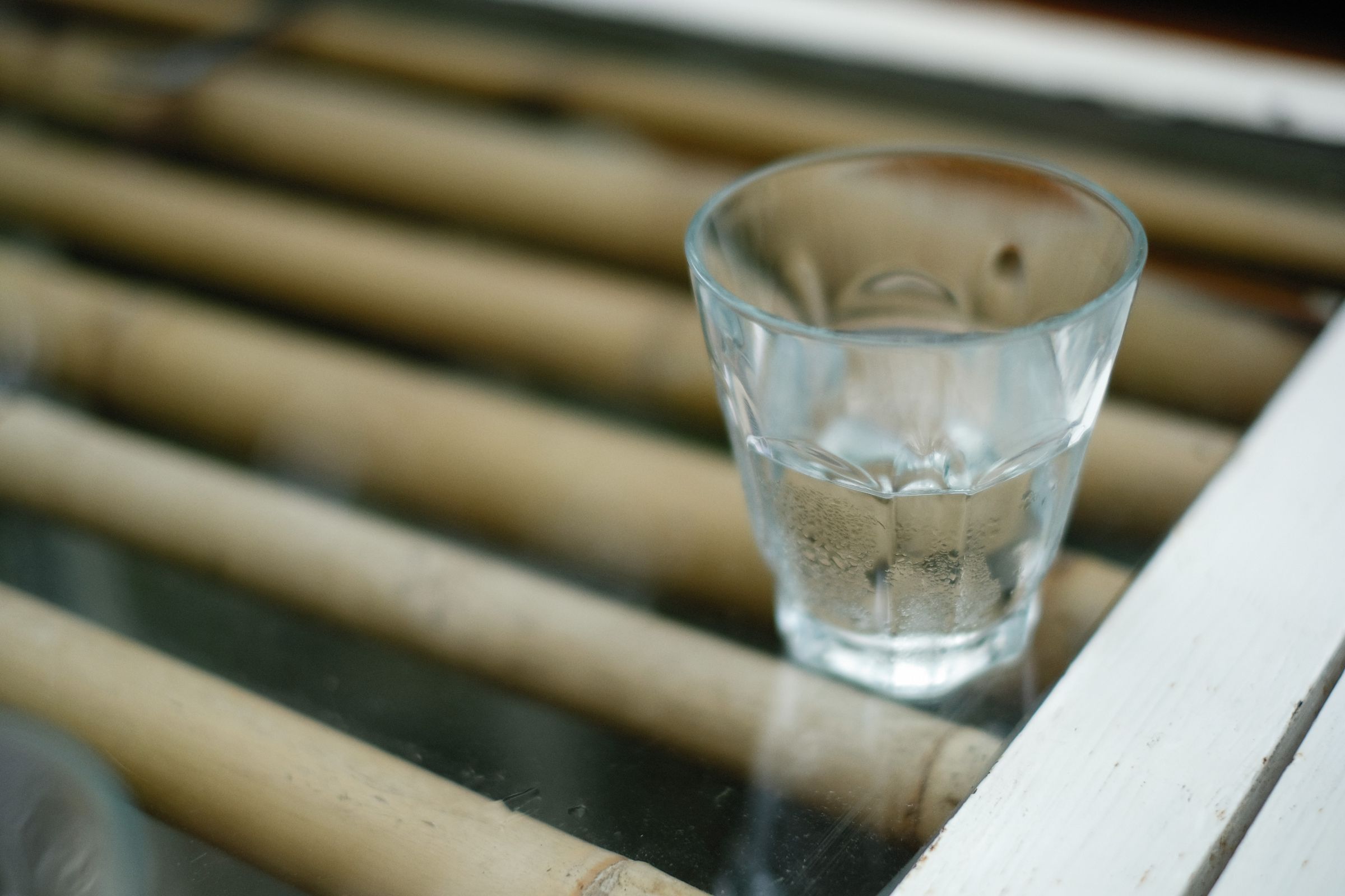 A clear drinking glass of water on a wooden slatted surface.