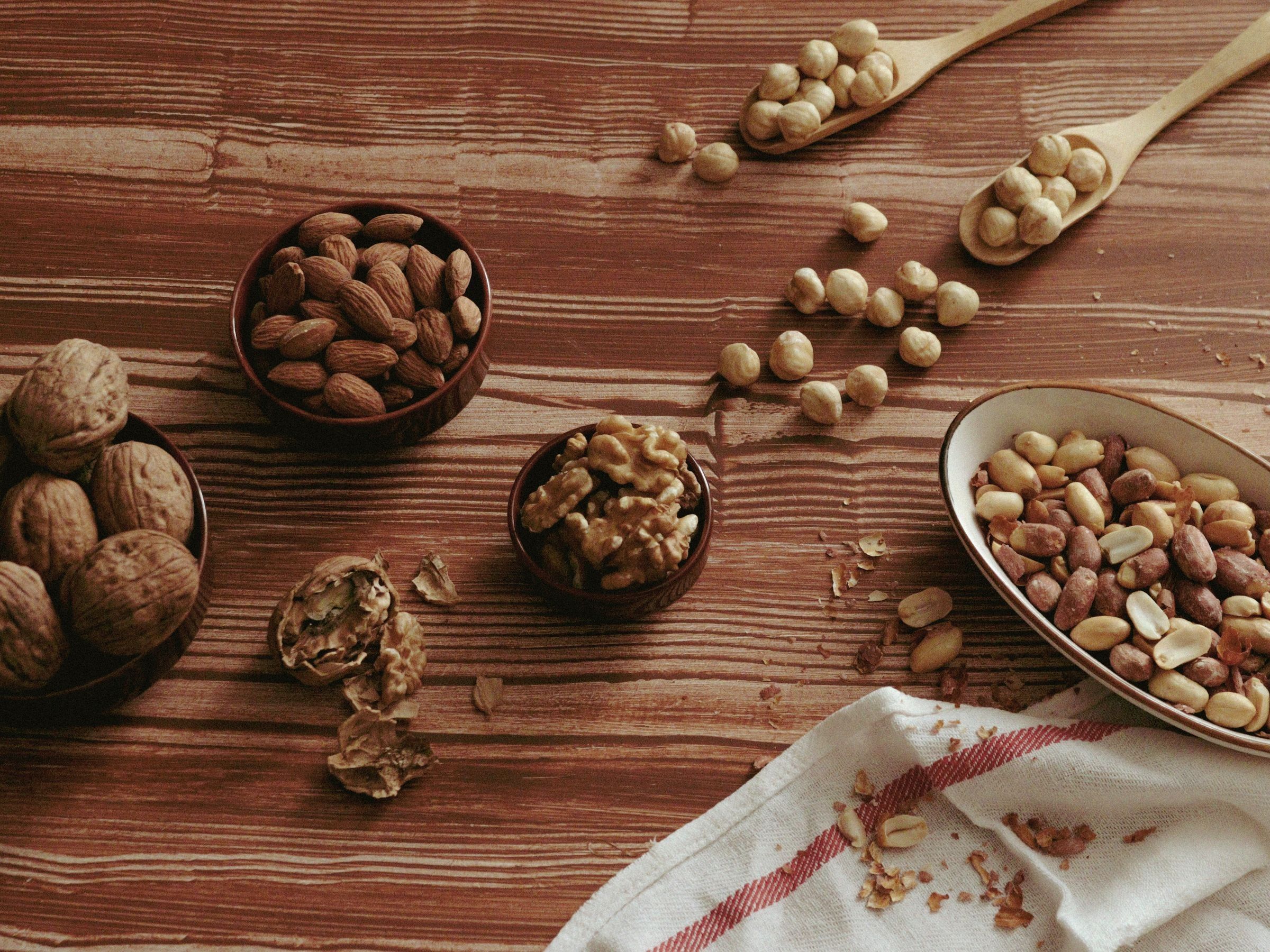Almonds, walnuts, shelled nuts and peanuts in wooden bowls and a dish on a brown wooden table.