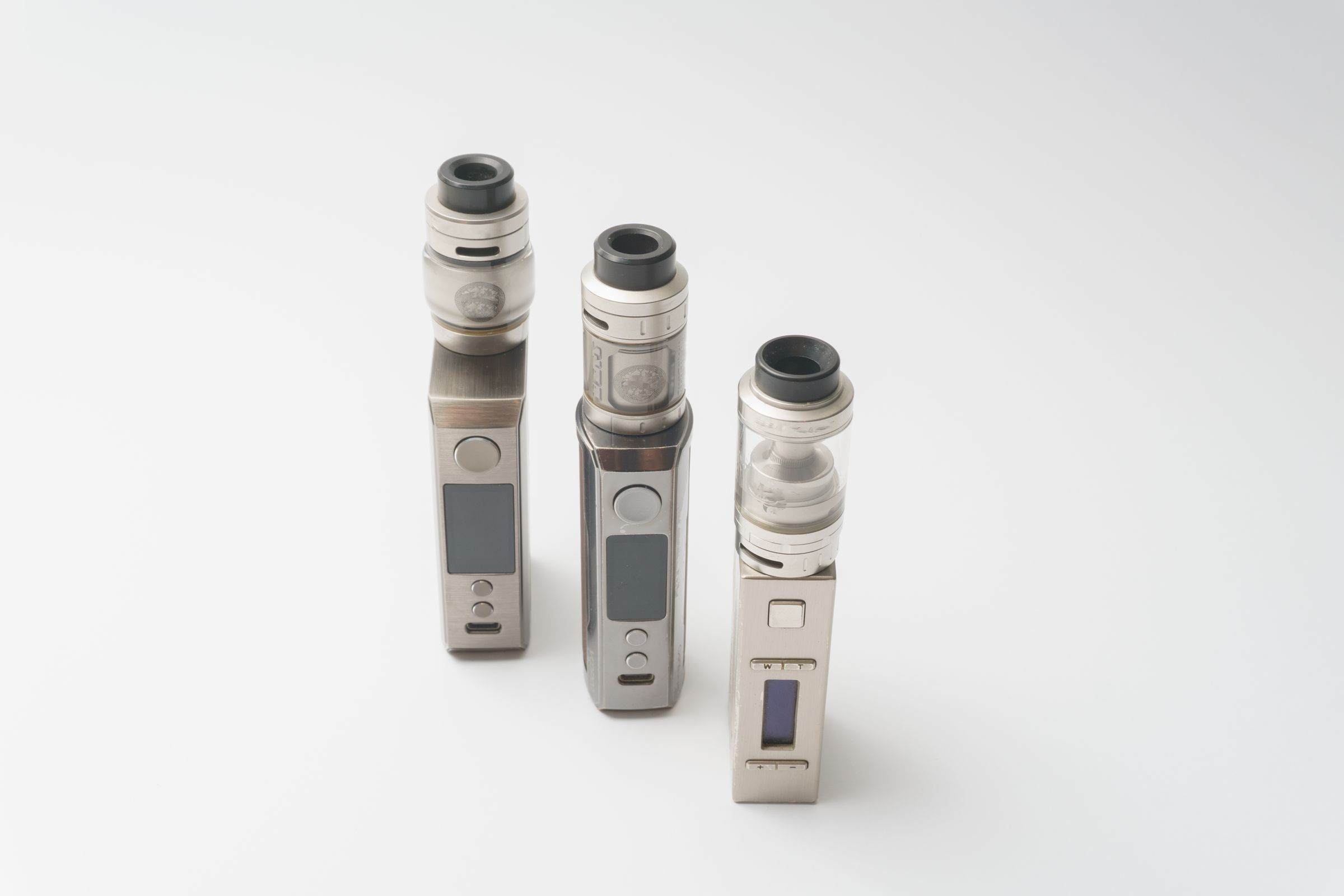 Three vape devices standing on a white surface.
