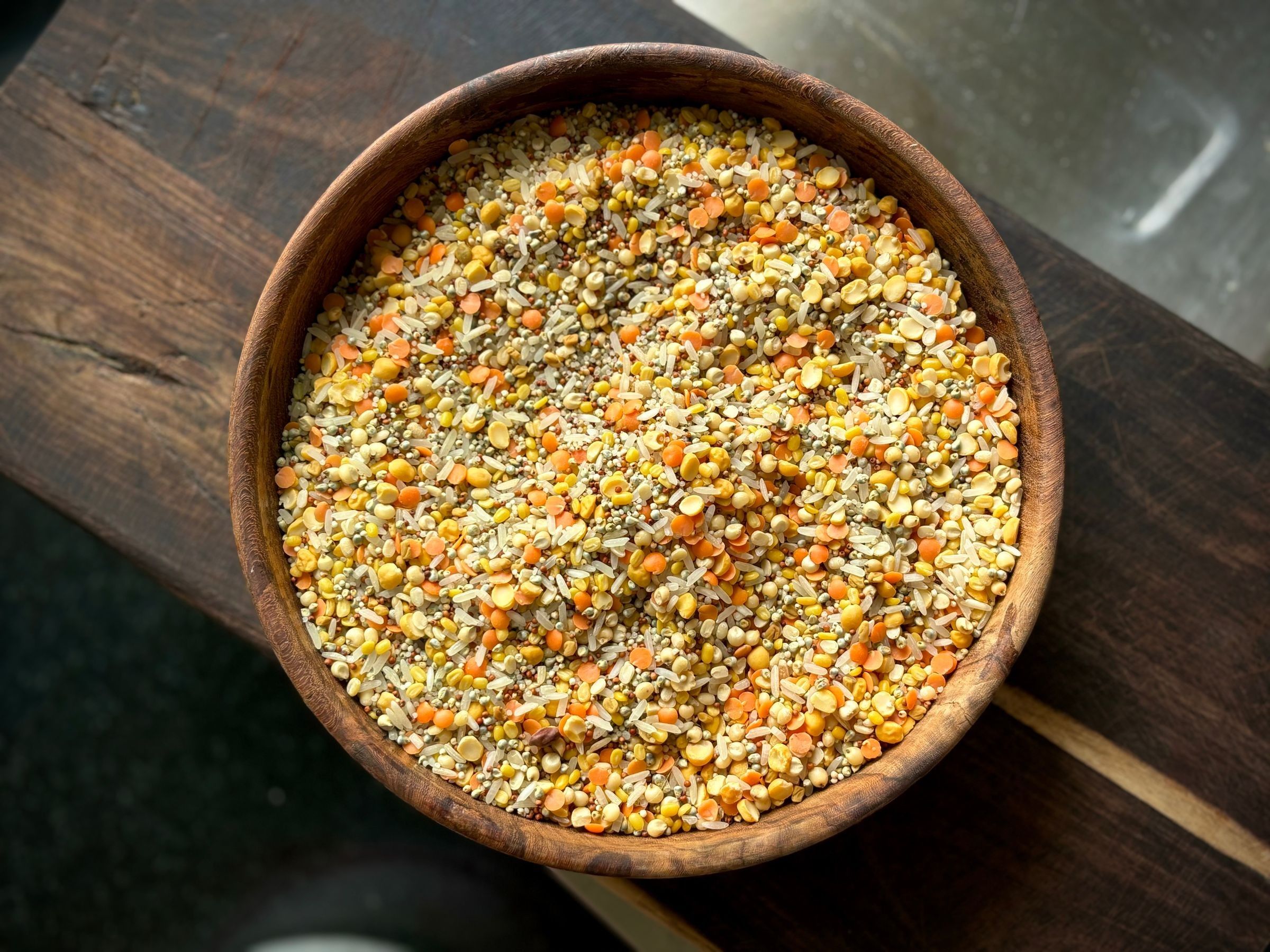 A wooden bowl filled with a mix of dried yellow, orange and green legumes.