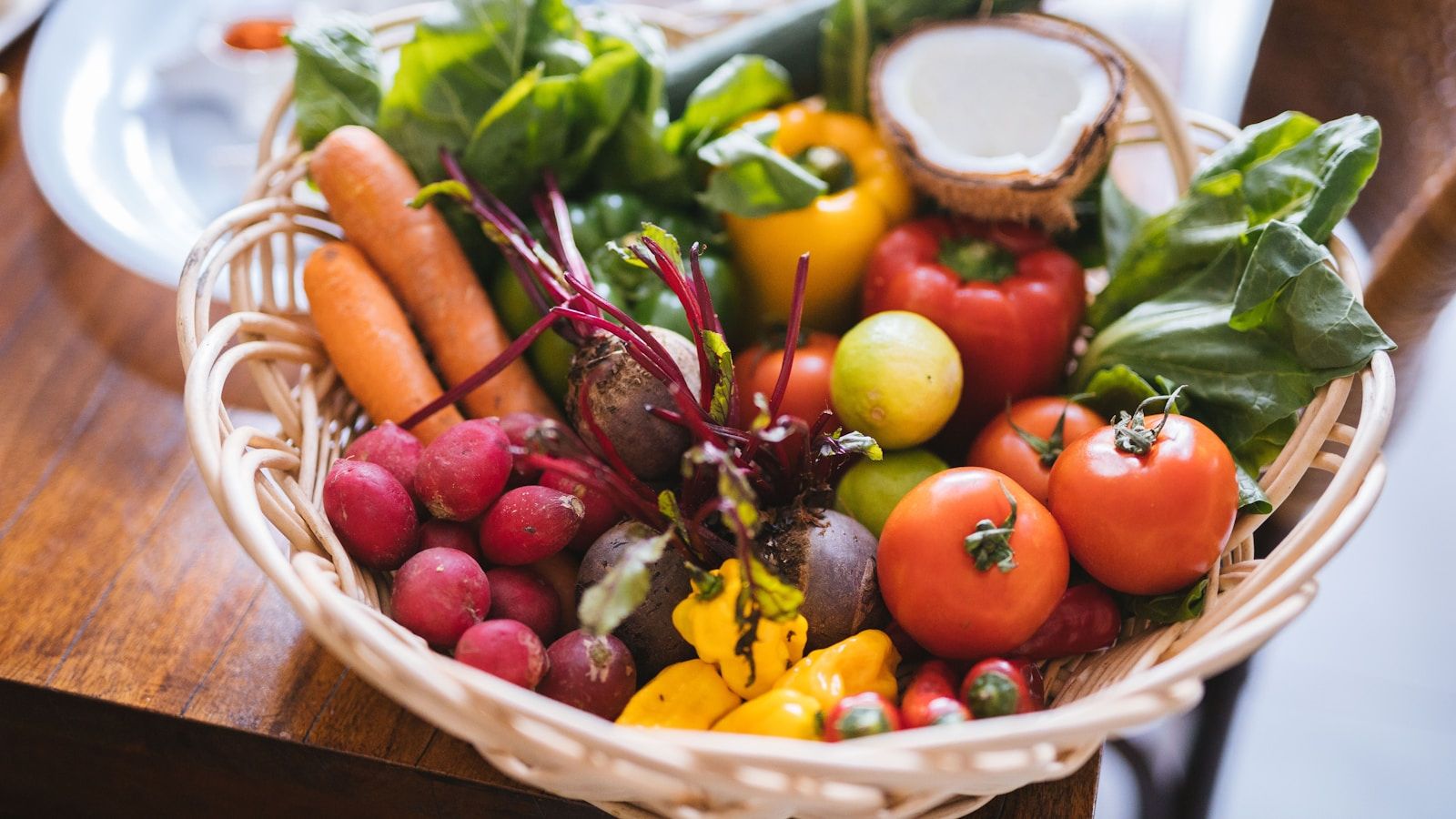 A wicker basket of fresh whole vegetables on a wooden table