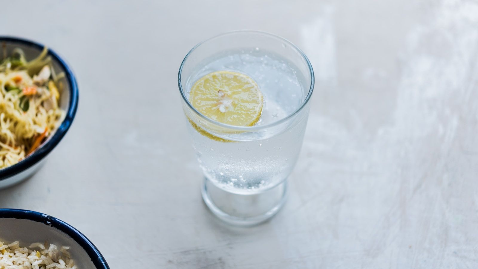A tall glass of sparkling water with a lemon slice on a white table