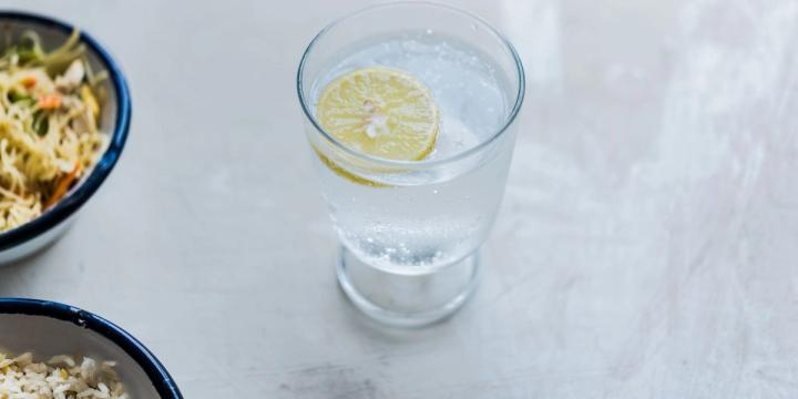 A tall glass of sparkling water with a lemon slice on a white table