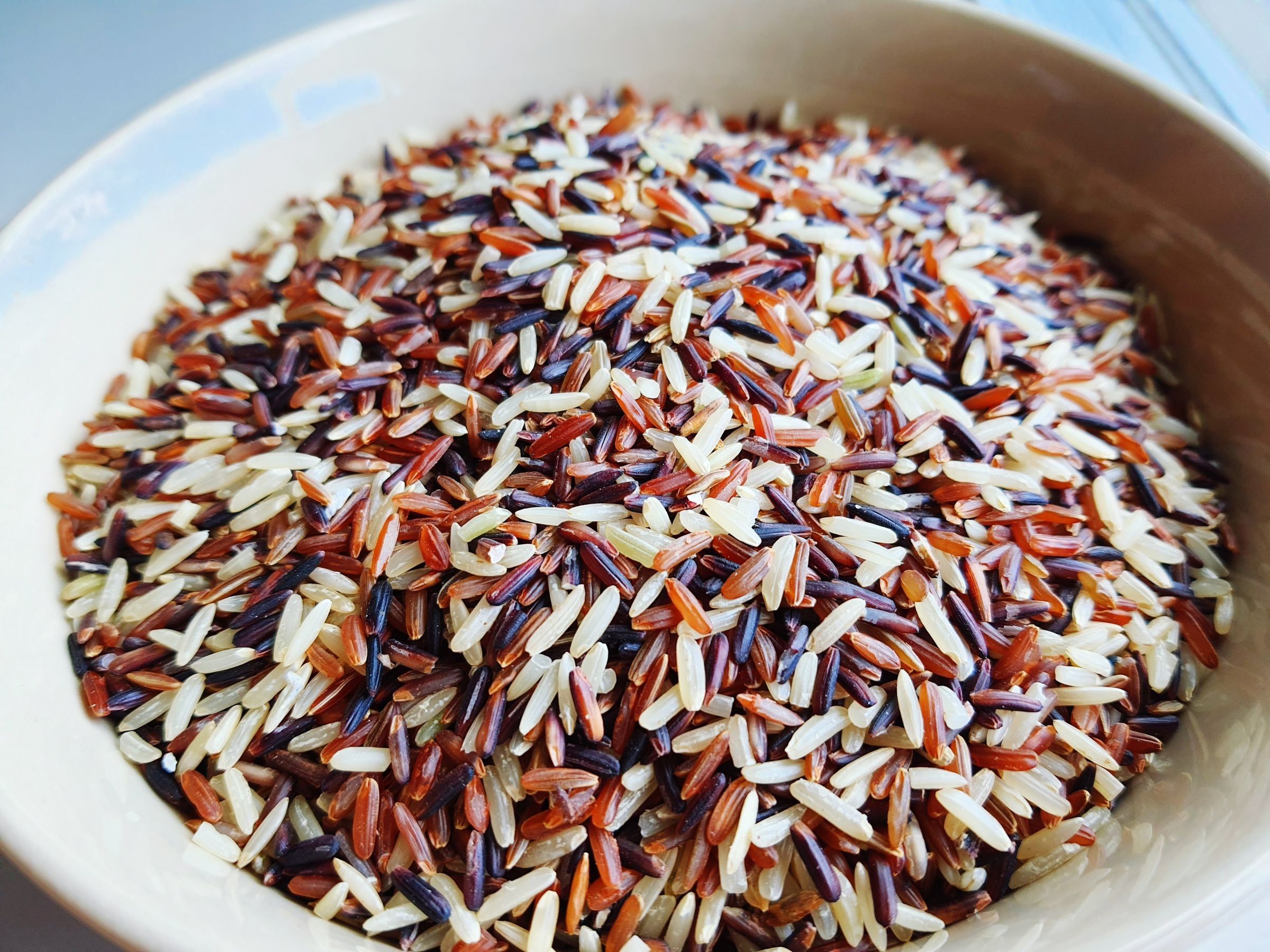 A bowl filled with mixed whole grain rice in white, brown, red and dark varieties.