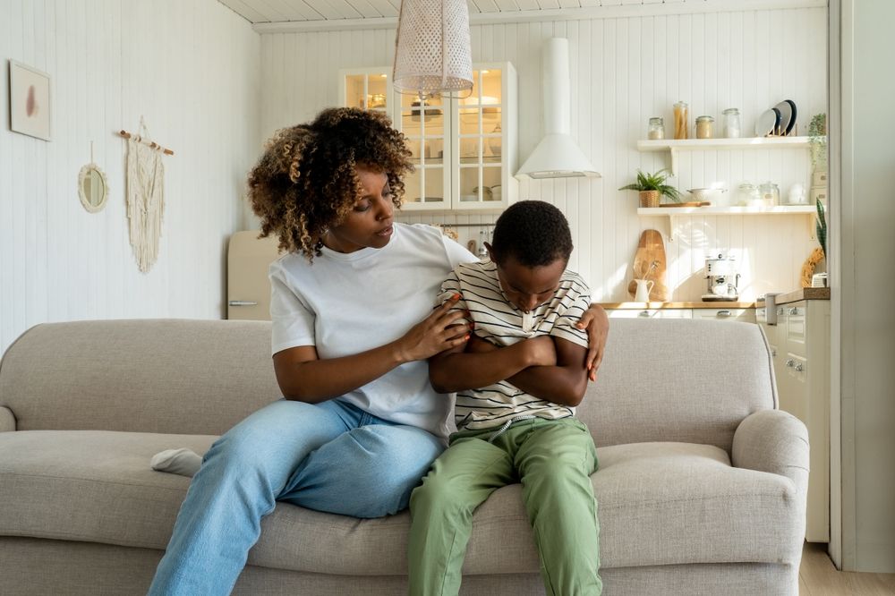 A mother comforting her upset child while sitting on a couch, representing families coping with harmful experiences on online platforms like Roblox.