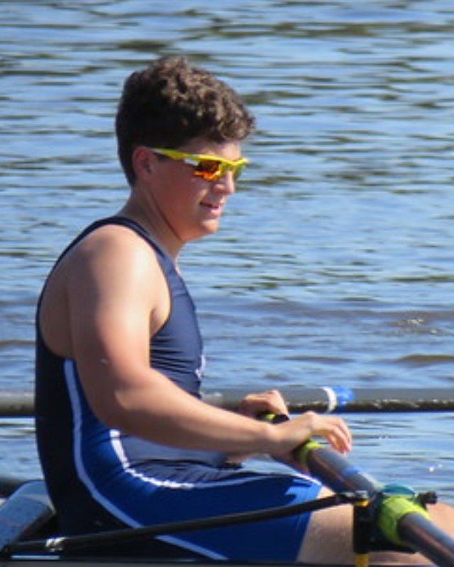 Nick rowing a single racing shell on open water, wearing sunglasses