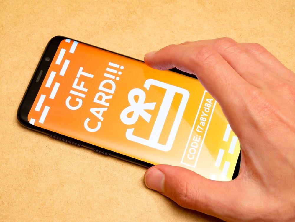 A person holding a smartphone displaying a digital gift card with a visible code, representing the Robux bait predators use to target children.