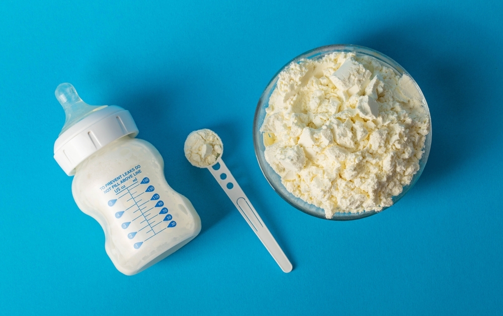 Image Baby bottle, formula powder, and measuring scoop on a blue background, representing concerns about the ByHeart infant formula recall and infant botulism outbreak.