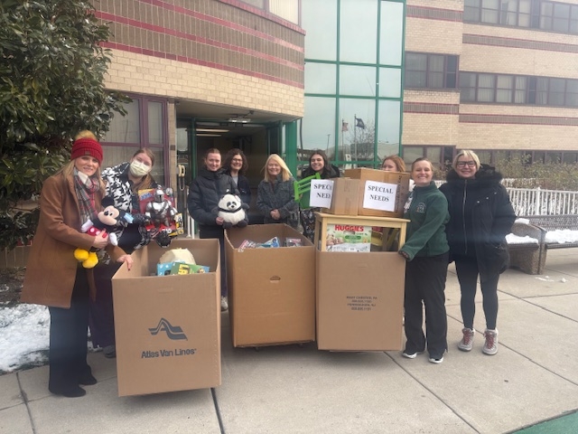 Image Anapol Weiss staff posing outside St. Christopher’s Hospital with large donation boxes containing toys, stuffed animals, and items specifically labeled for the "SPECIAL NEEDS" wishlist, including a small green chair and diapers, as part of their 2025 holiday initiative.
