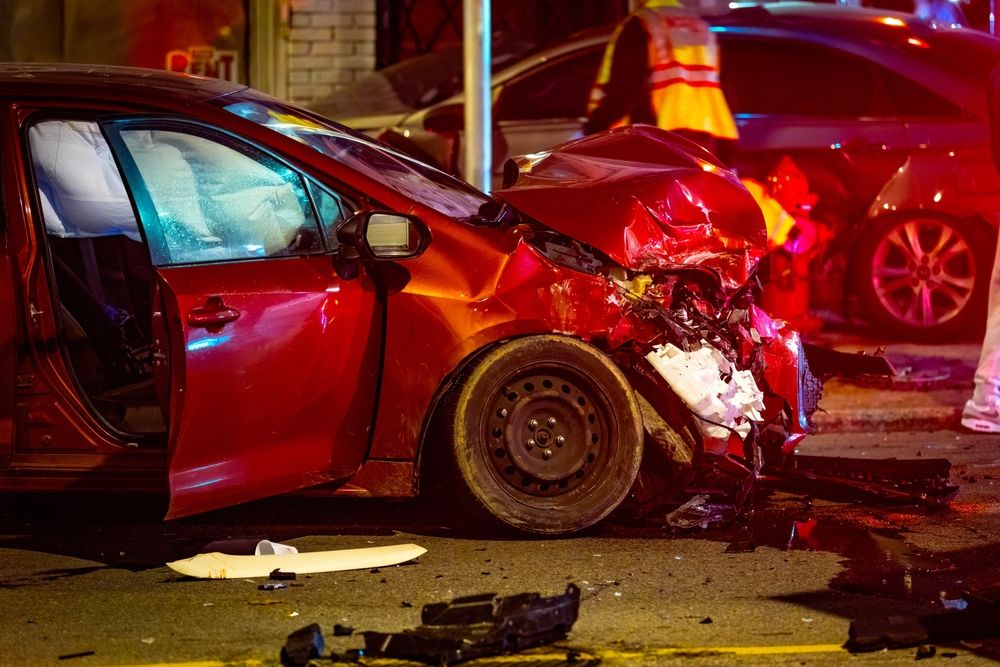 A severe front-end car accident involving a red sedan with deployed airbags on a city street at night during the December holiday season.