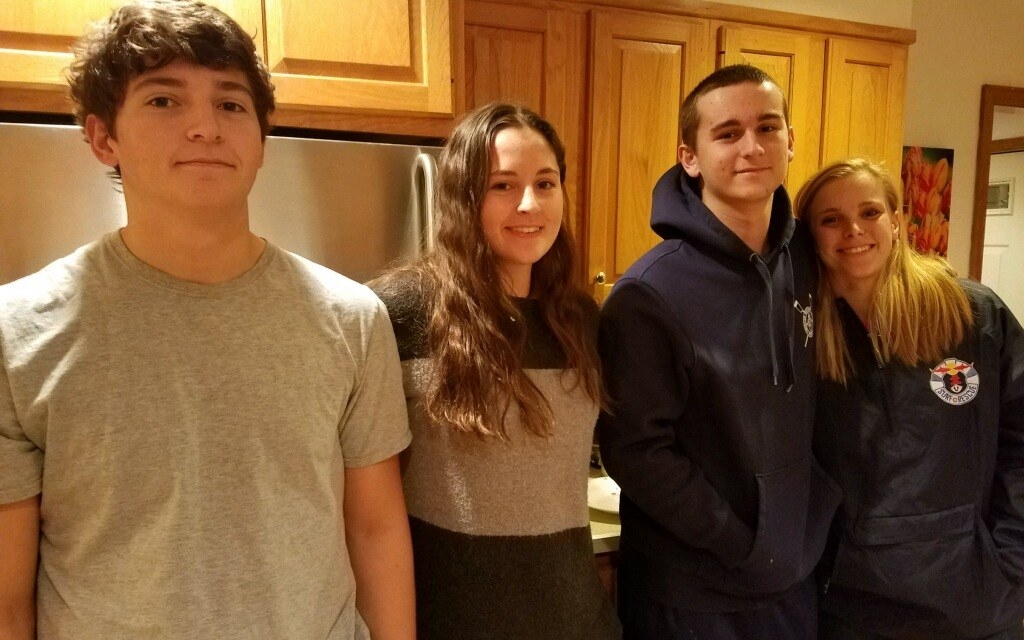 Nick with three other teenagers, arms around each other in a kitchen