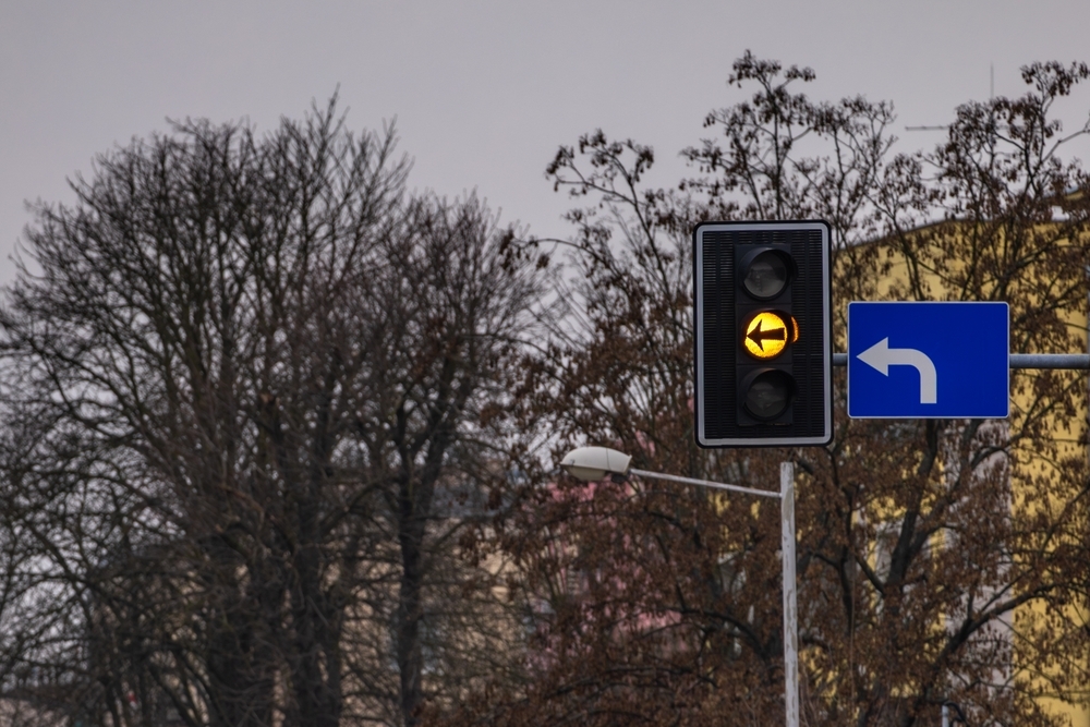 Image A yellow left-turn arrow traffic signal and blue directional sign set against bare winter trees, symbolizing the hazards of holiday shopping traffic.