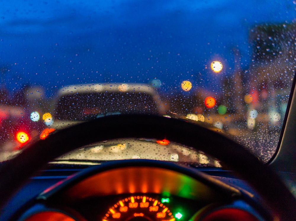 View through a rainy car windshield at night, showing blurred traffic and holiday lights, illustrating the hazards of distracted driving and gridlock during the festive season.