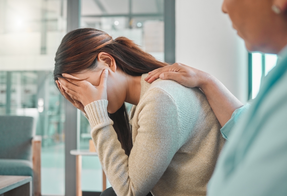 Image Distressed woman holding her head while another person offers support, representing pain and complications after breast surgery