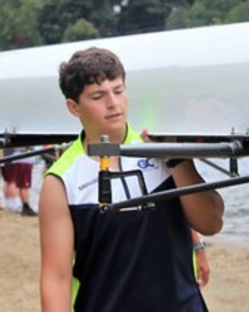 Nick carrying a rowing shell on his shoulder at the water's edge