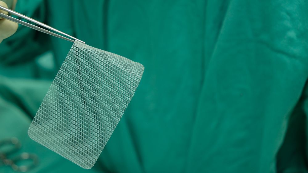 Surgical mesh held with medical instrument in operating setting representing breast mesh risks and complications