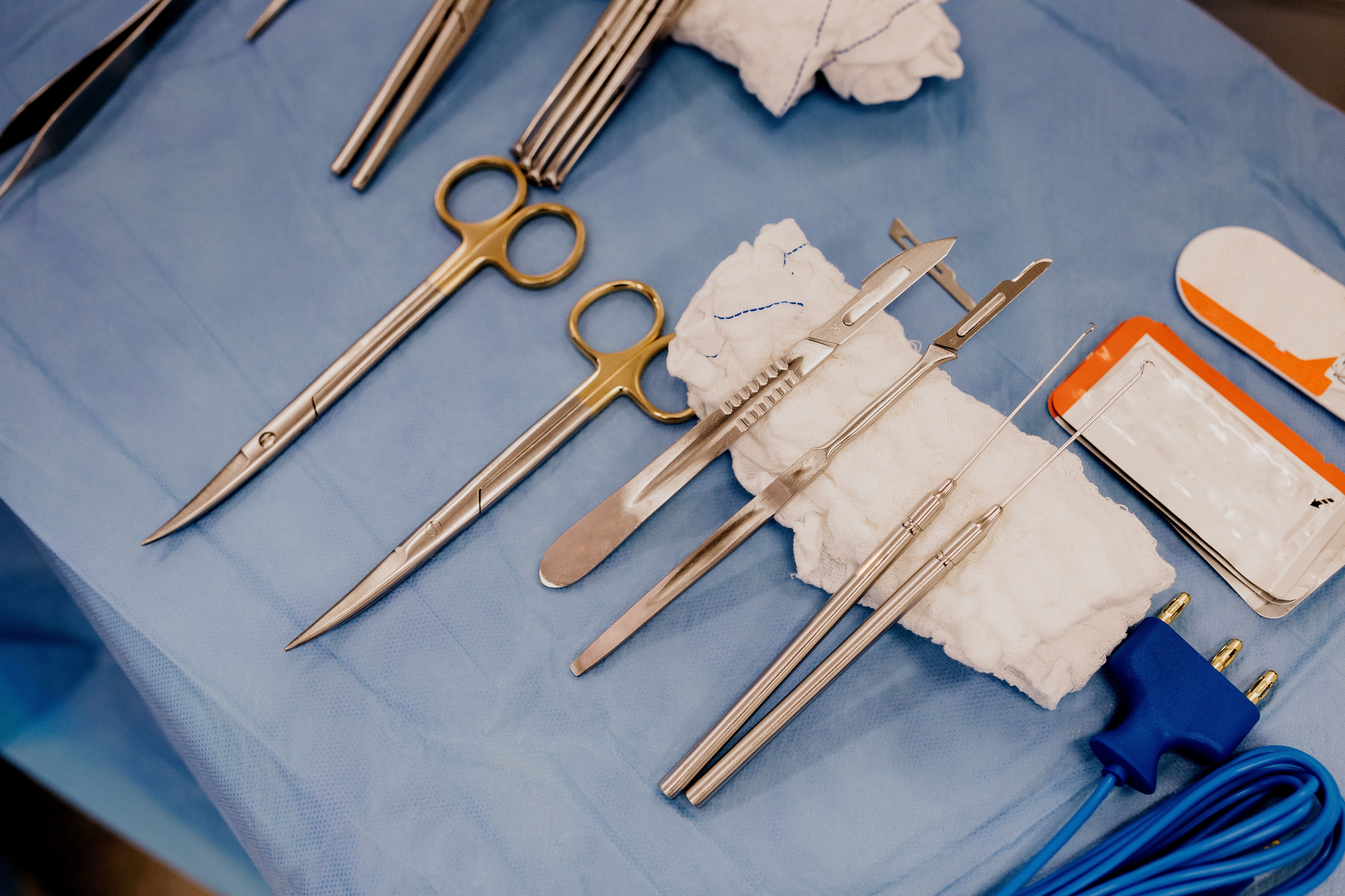 Image Sterile surgical instruments including scissors, clamps, forceps, and a suture needle laid out on a blue surgical drape before an operation