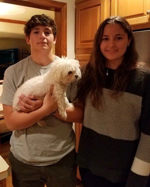 Nick holding a small white dog, standing beside a young woman