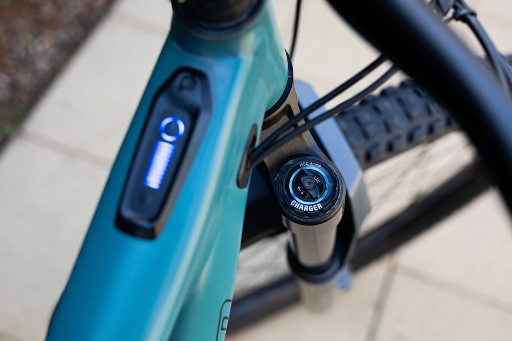 Image Close-up top-down view of a teal electric mountain bike frame, showing the digital display screen on the top tube and the front suspension adjustment dial.
