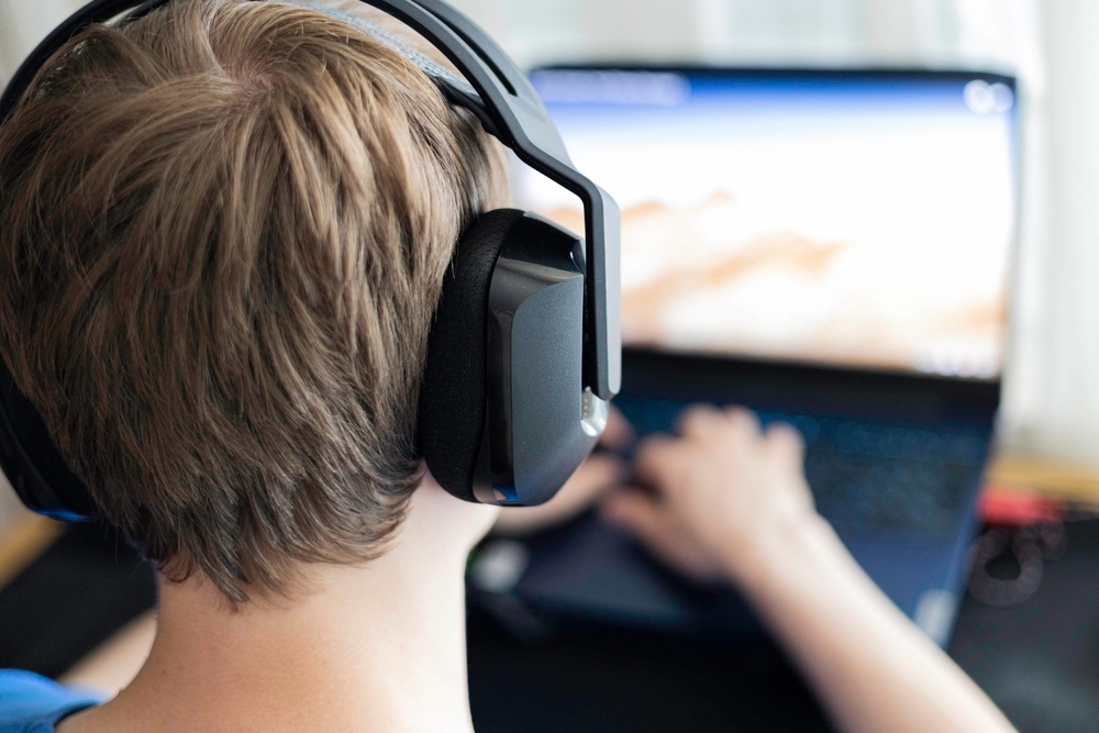 Image A teenager with headphones using a laptop, illustrating the digital environments where the 764 network targets children on platforms like Roblox.