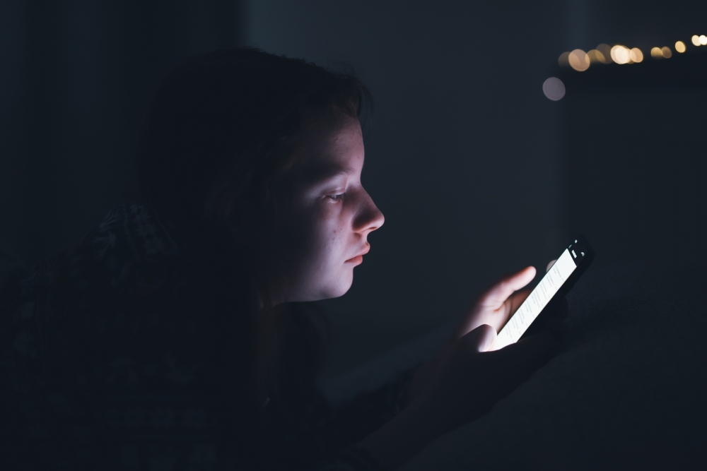 Image Teen using a smartphone at night illustrating risks of online sexual harassment and unsafe interactions on social media platforms