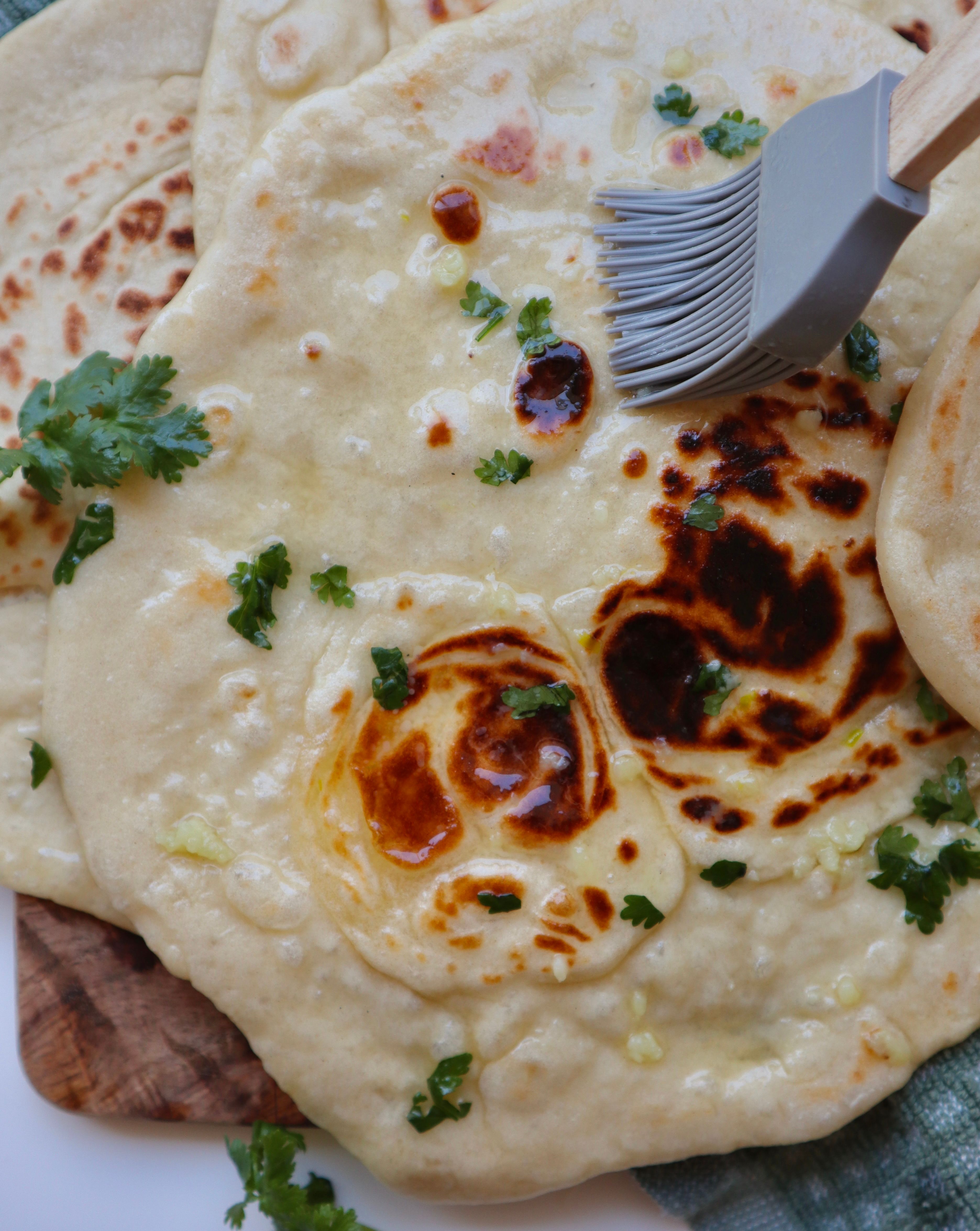 Brushing garlic butter onto freshly cooked naan bread with a pastry brush and fresh herbs.