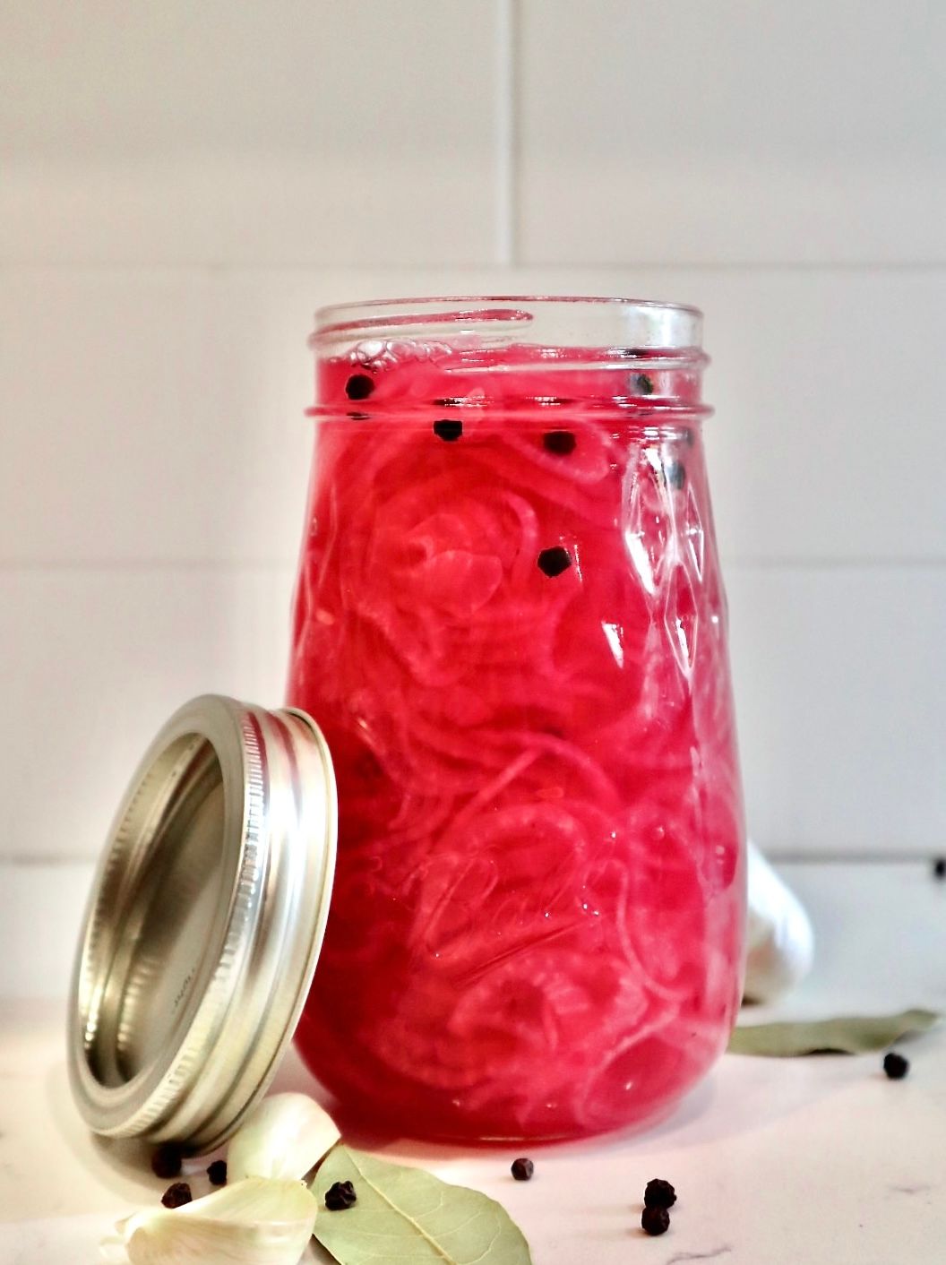 Jar of homemade pickled red onions with peppercorns and garlic on kitchen counter.