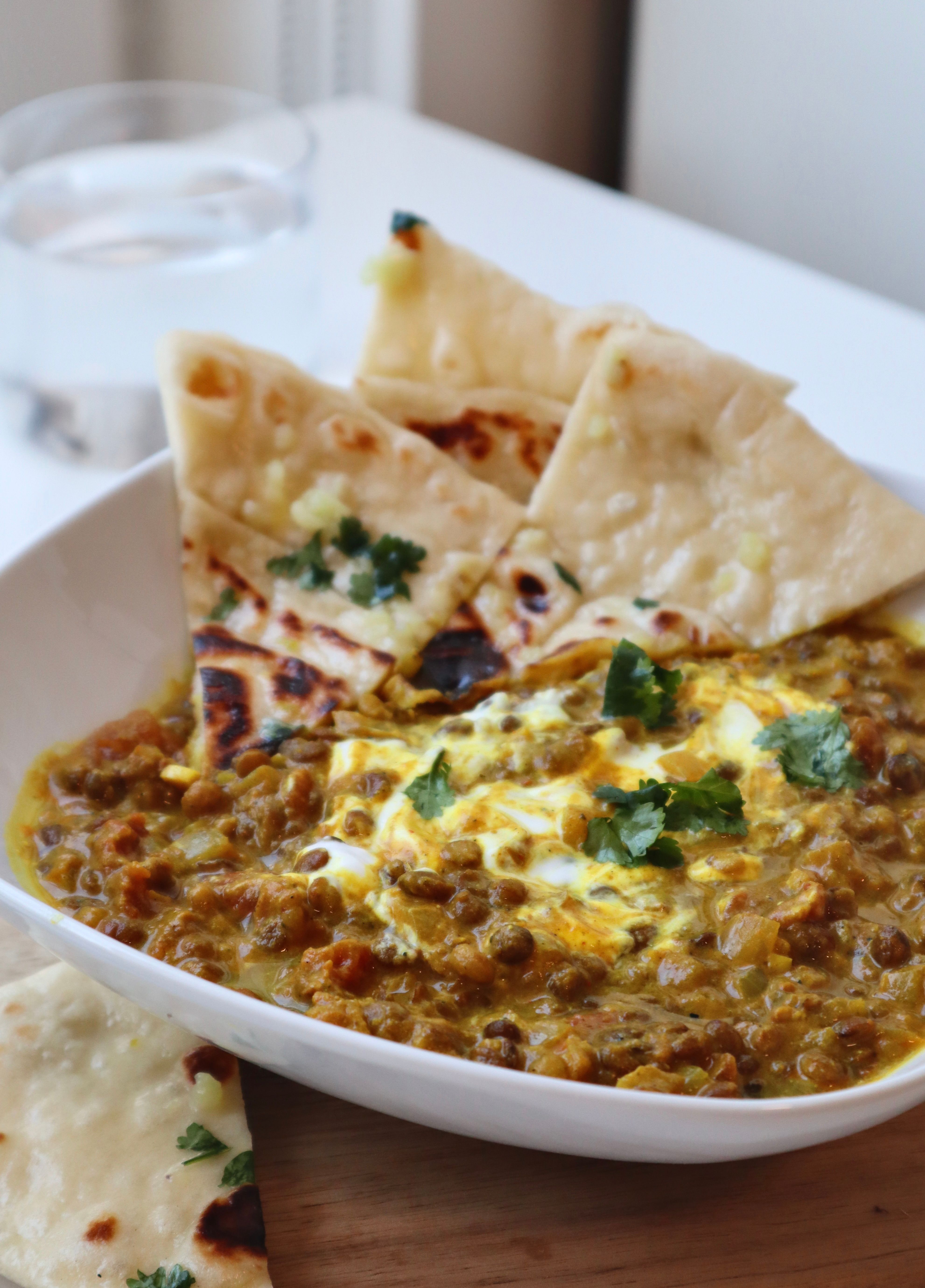 Vegetarian dinner bowl with Indian red lentil daal, topped with plain yogurt and chopped cilantro, and garlic naan.