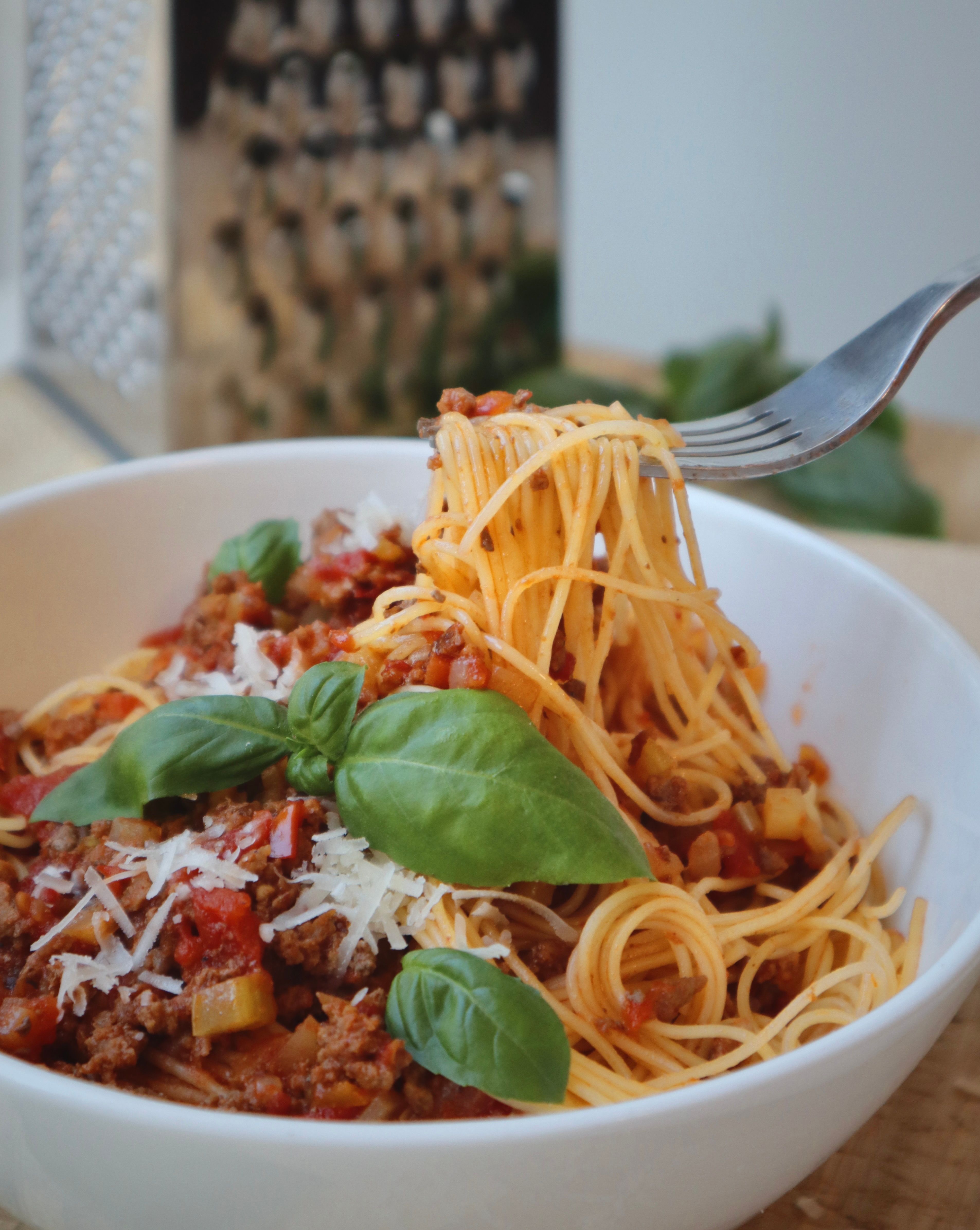 Fork twirling spaghetti bolognese with meat sauce, basil, and parmesan in a white bowl