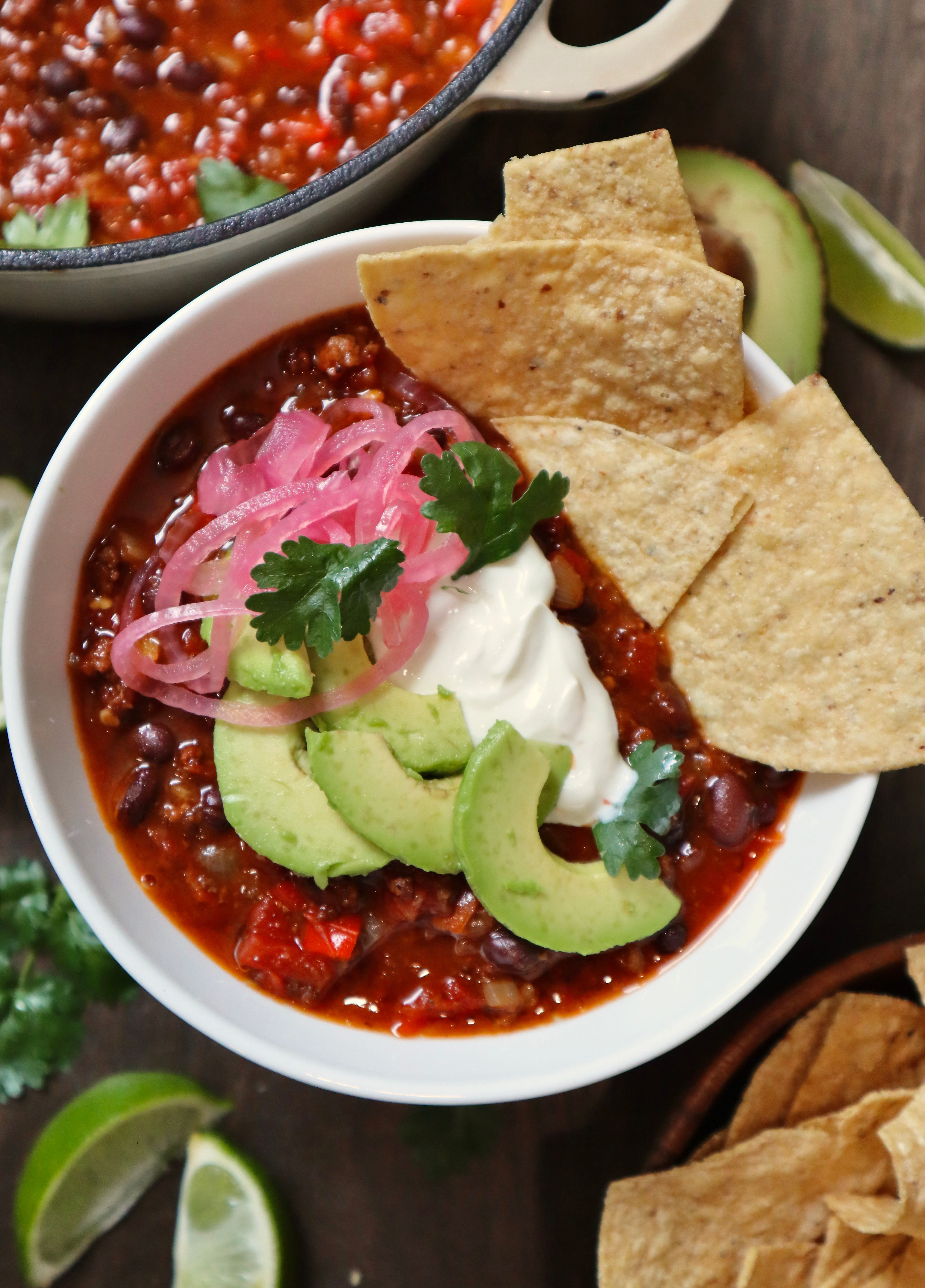 Bowl of chili con carne with tortilla chips, avocado, sour cream, and pickled onions
