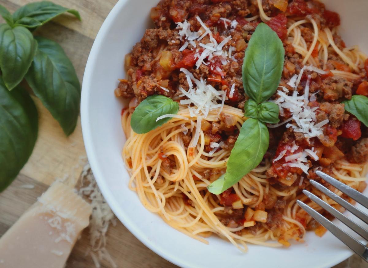 Spaghetti bolognese served in a white bowl with fresh basil and grated parmesan on a wooden board
