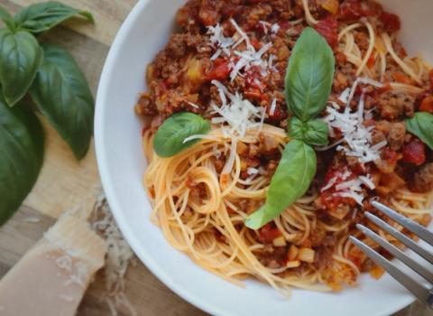 Spaghetti bolognese served in a white bowl with fresh basil and grated parmesan on a wooden board
