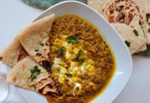 Bowl of Indian red lentil daal dinner, topped with natural greek yoghurt and cilantro and served with garlic naan bread