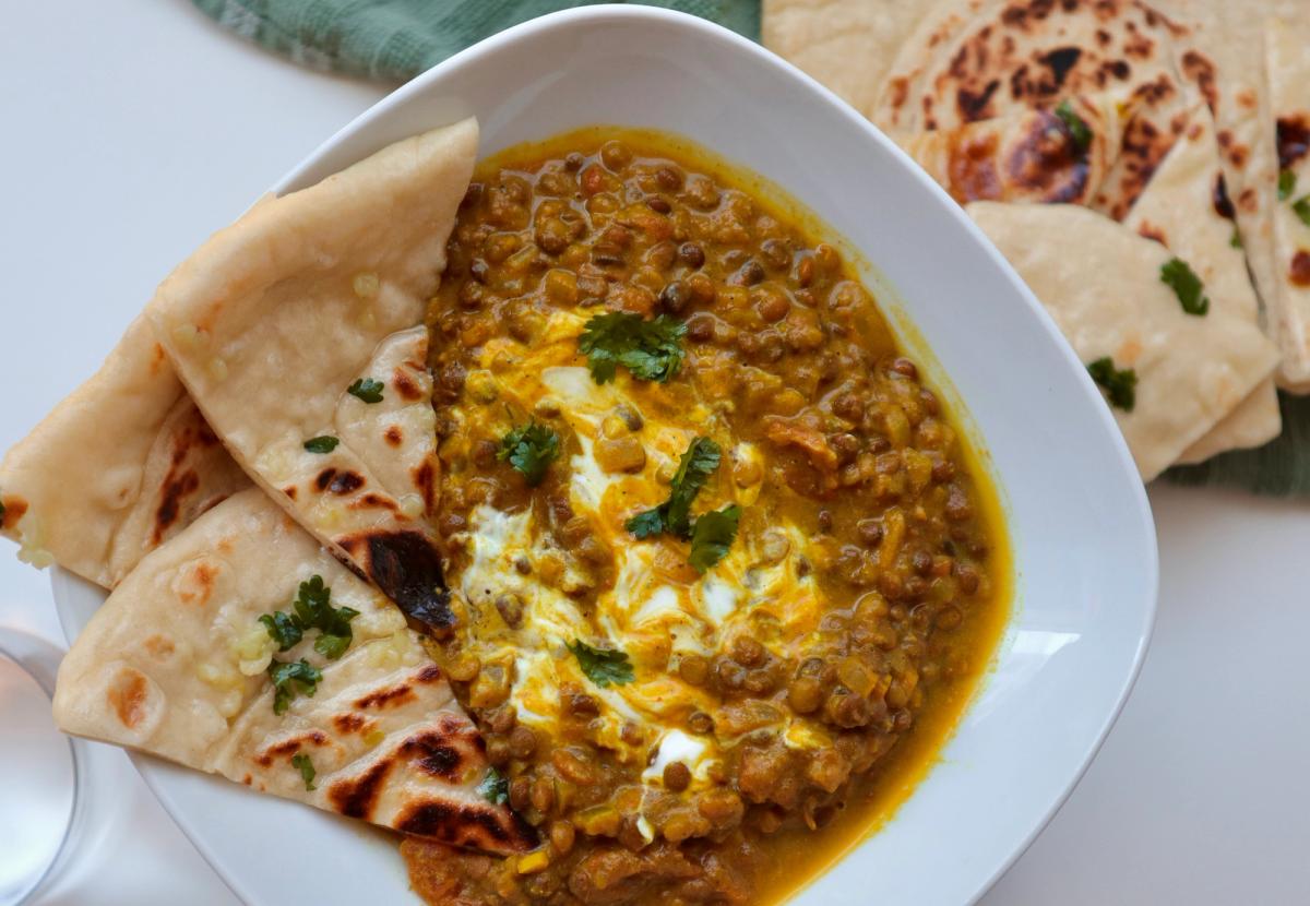 Bowl of Indian red lentil daal dinner, topped with natural greek yoghurt and cilantro and served with garlic naan bread