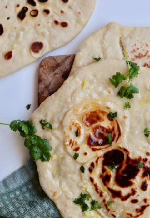 Homemade plain and garlic naan bread brushed with butter and topped with fresh cilantro, served on a wooden plate.