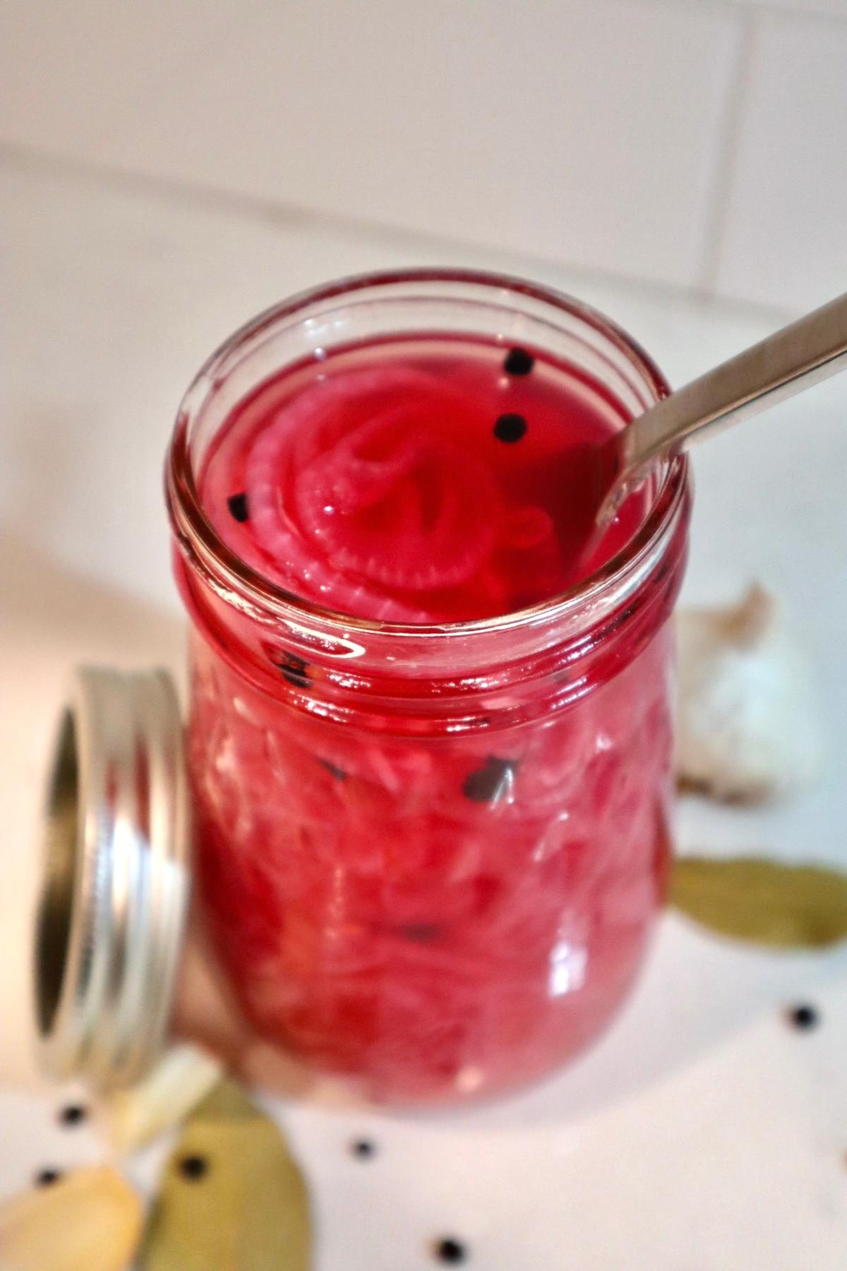 Jar of homemade pickled red onions with peppercorns and garlic
