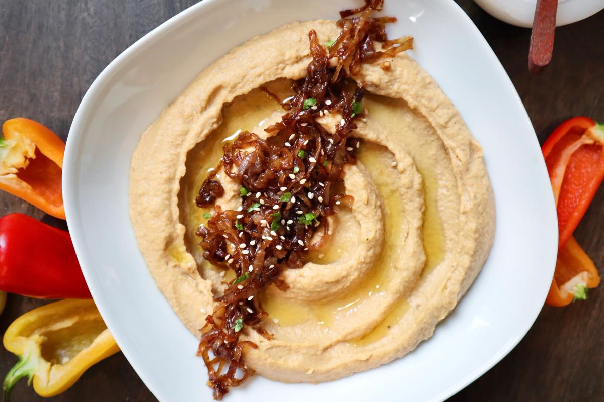 Caramelized onion hummus topped with olive oil in white bowl and served with mini bell peppers.