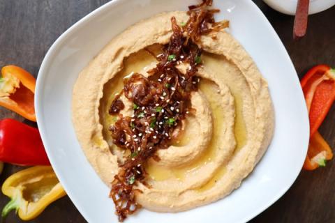 Caramelized onion hummus topped with olive oil in white bowl and served with mini bell peppers.